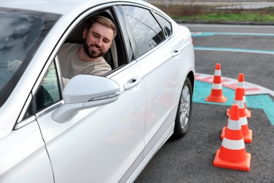 Photo of Young man in car on test track with traffic cones. Driving school