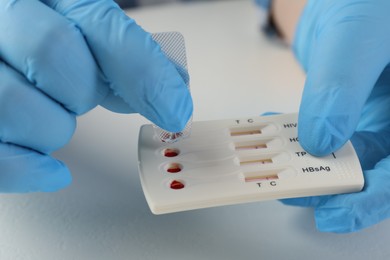Doctor dropping buffer solution onto disposable multi-infection express test cassette at white table, closeup