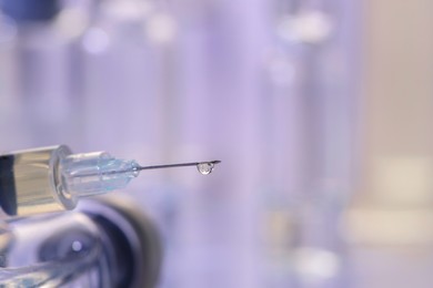 Photo of Drop of medication on syringe needle against blurred background, closeup. Space for text