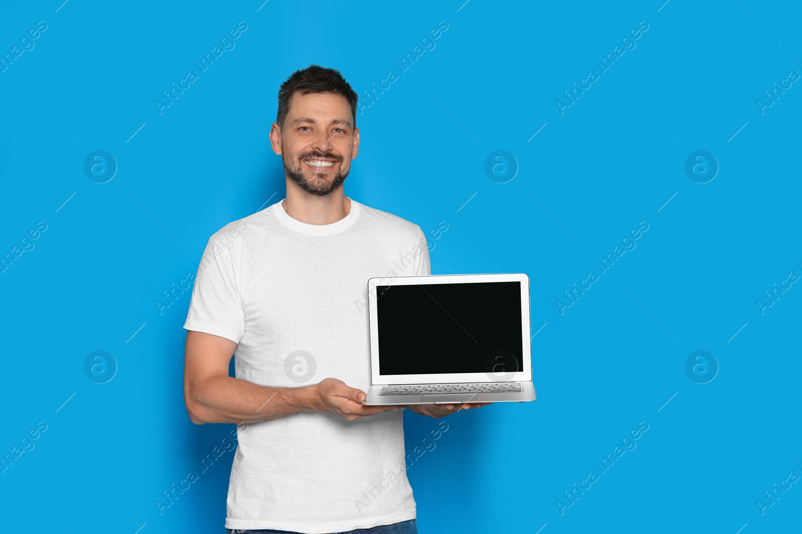 Photo of Happy man holding laptop on light blue background. Space for text