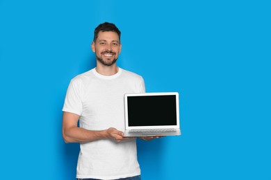 Photo of Happy man holding laptop on light blue background. Space for text