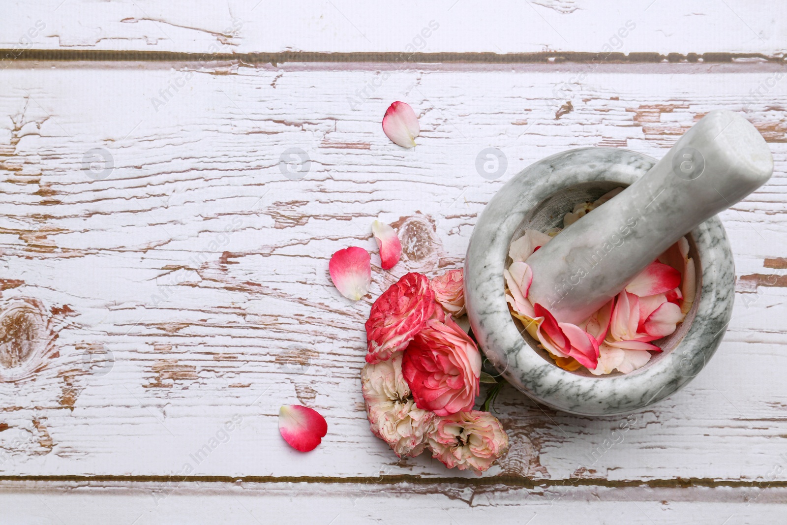 Photo of Mortar with pestle and rose petals on white wooden table, flat lay. Space for text