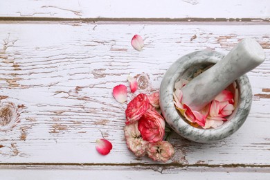 Photo of Mortar with pestle and rose petals on white wooden table, flat lay. Space for text