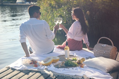 Couple clinking glasses with wine on pier at picnic, back view
