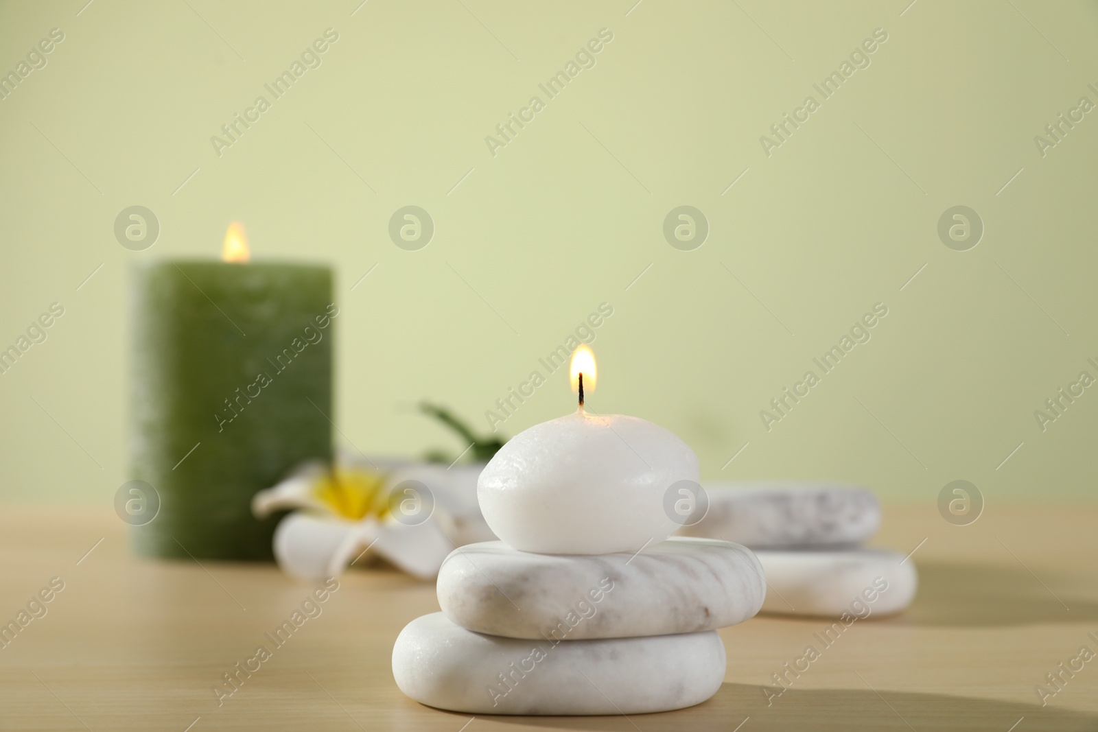 Photo of Spa stones and burning candles on wooden table against light green background