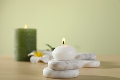 Photo of Spa stones and burning candles on wooden table against light green background