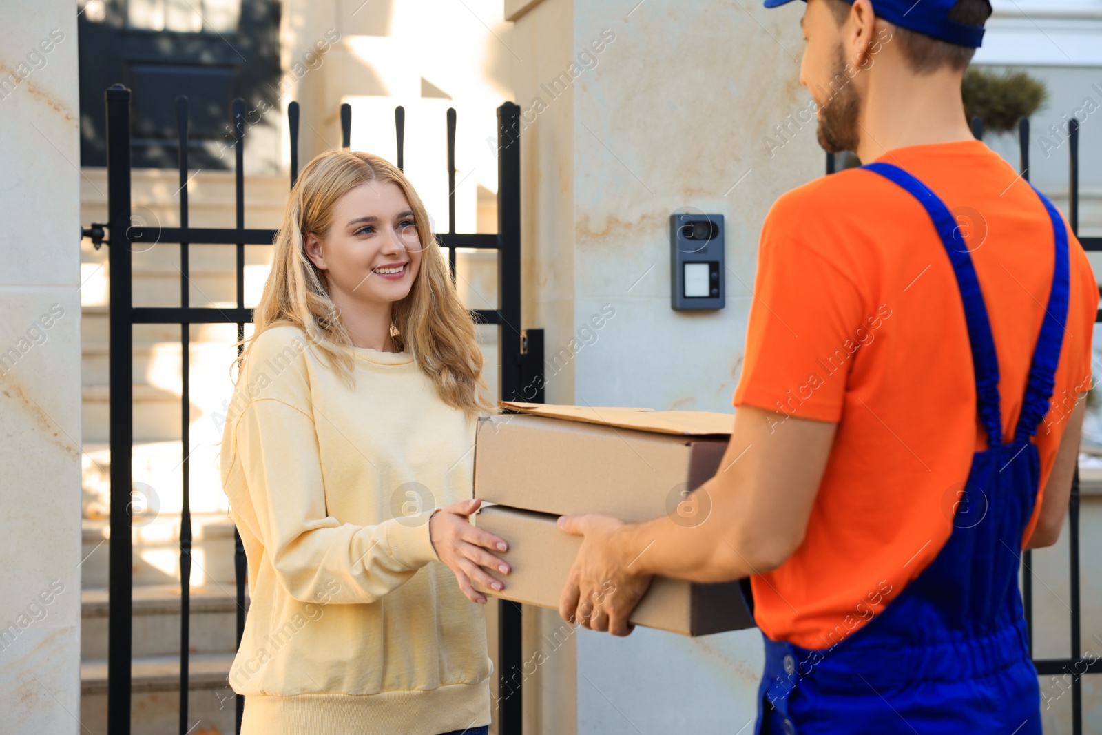 Photo of Woman accepting parcels from courier in uniform outdoors