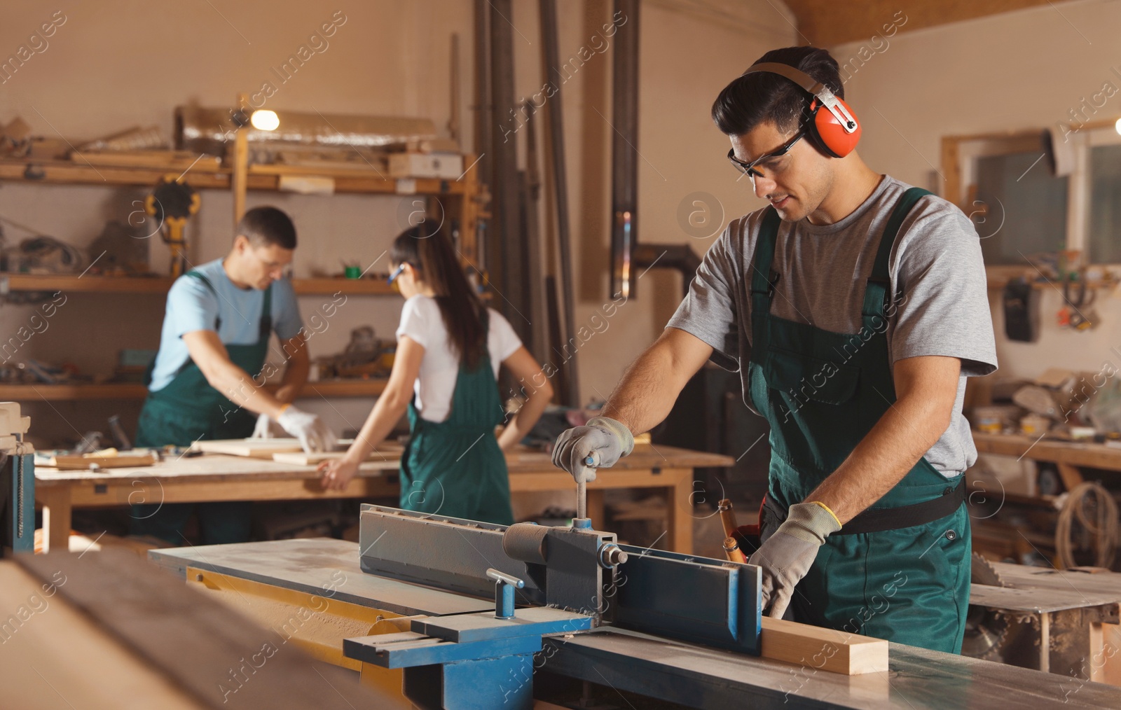 Photo of Professional carpenter working with surface planer and colleagues in workshop