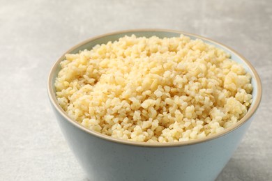 Delicious bulgur in bowl on light grey table, closeup