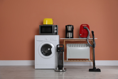 Photo of Set of different home appliances with vacuum cleaner near brown wall indoors