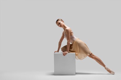 Young ballerina practicing dance moves on cube against white background. Space for text