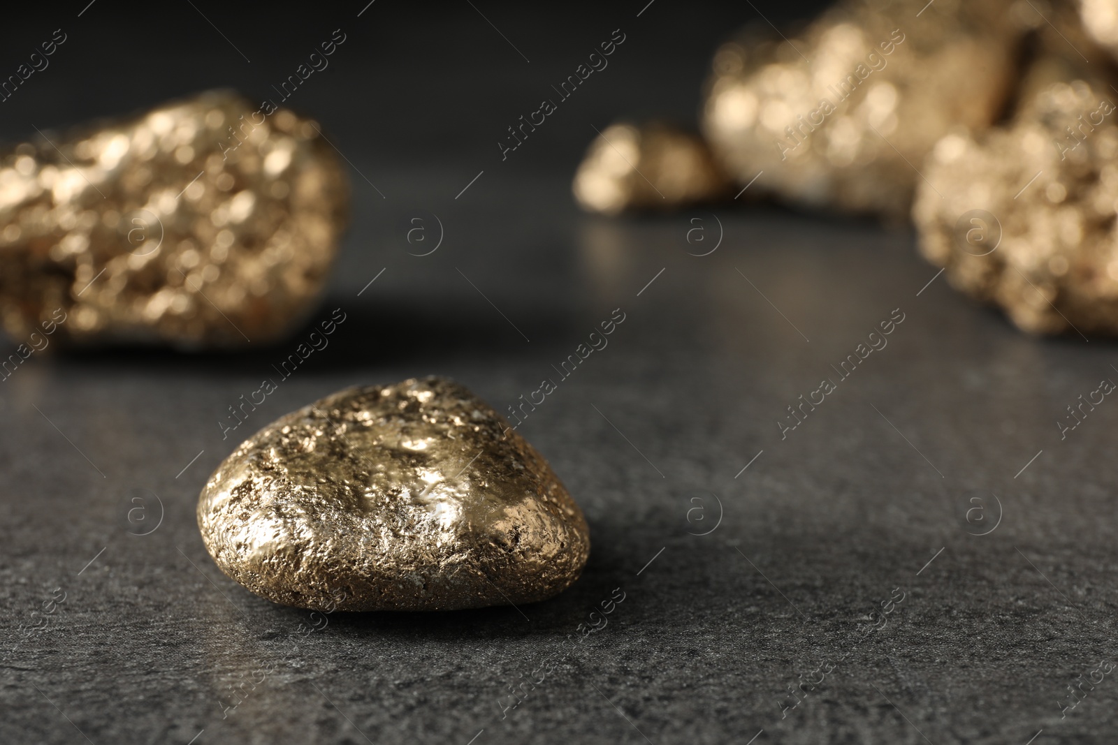 Photo of Shiny gold nugget on grey surface, closeup. Space for text