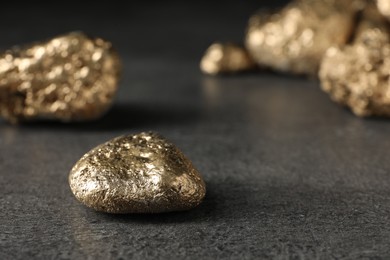 Photo of Shiny gold nugget on grey surface, closeup. Space for text