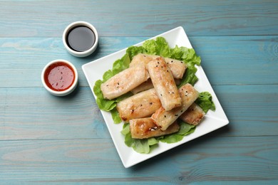 Photo of Tasty fried spring rolls, lettuce and sauces on light blue wooden table, flat lay