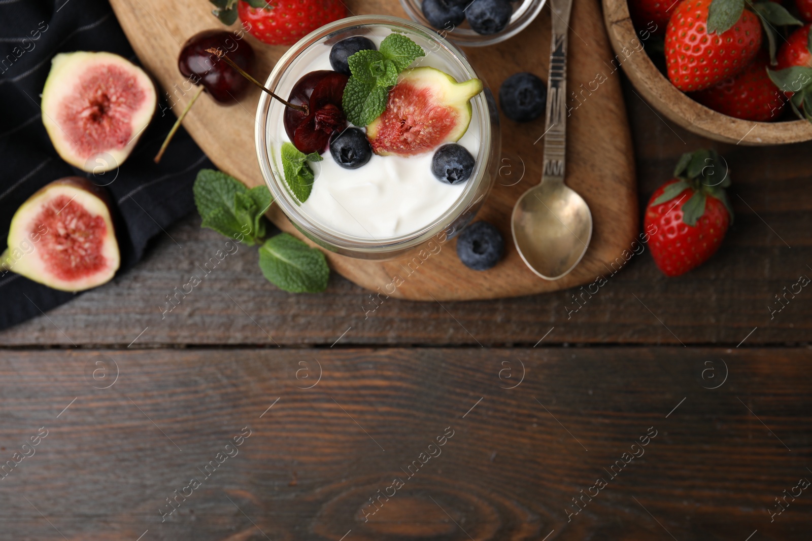 Photo of Glass with yogurt, berries and mint on wooden table, top view. Space for text