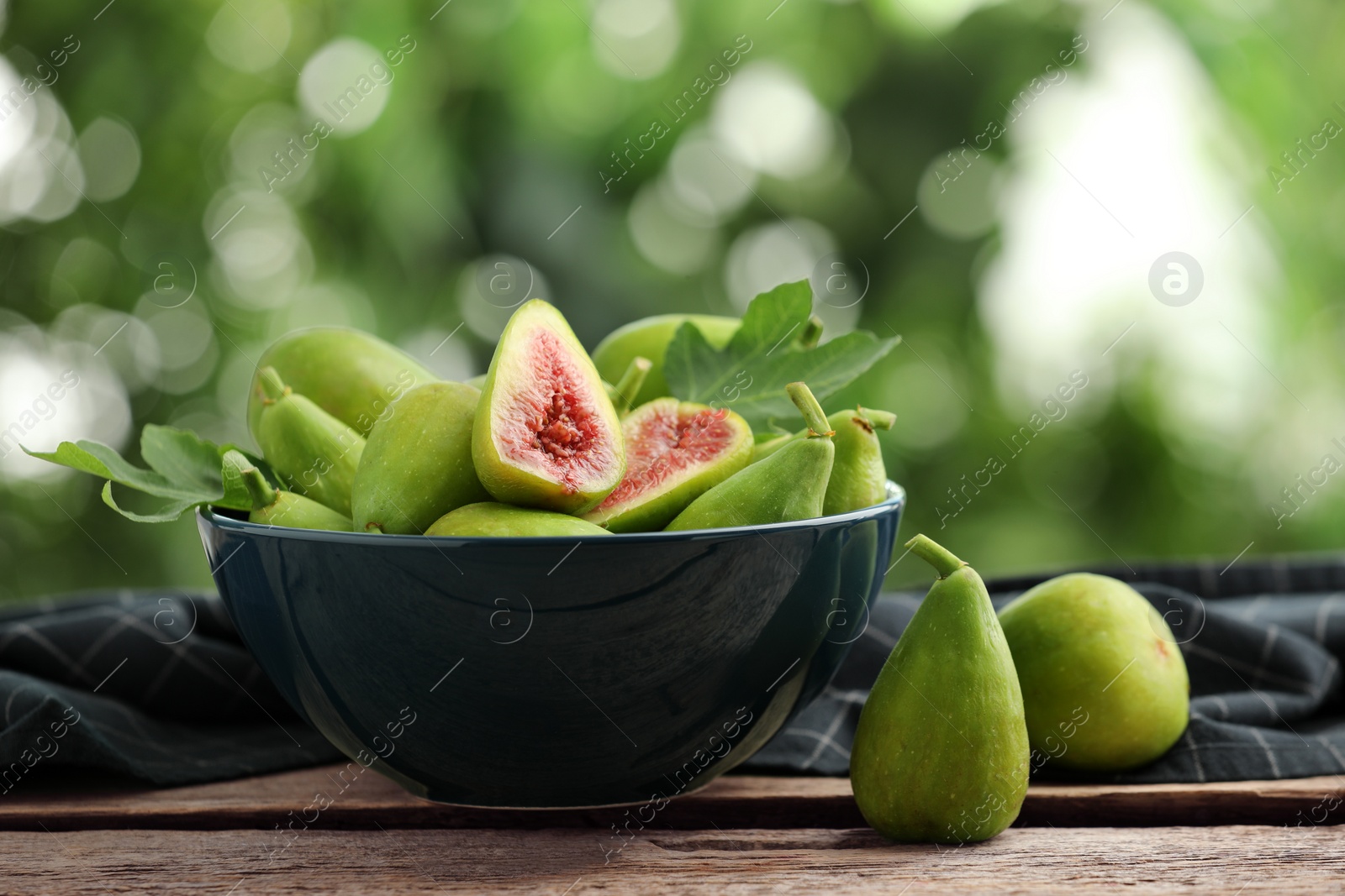 Photo of Cut and whole green figs on wooden table against blurred background, space for text