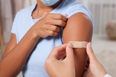Photo of Doctor putting adhesive bandage on young woman's arm after vaccination indoors, closeup