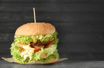 Photo of Burger with delicious patty on gray table against dark background, space for text