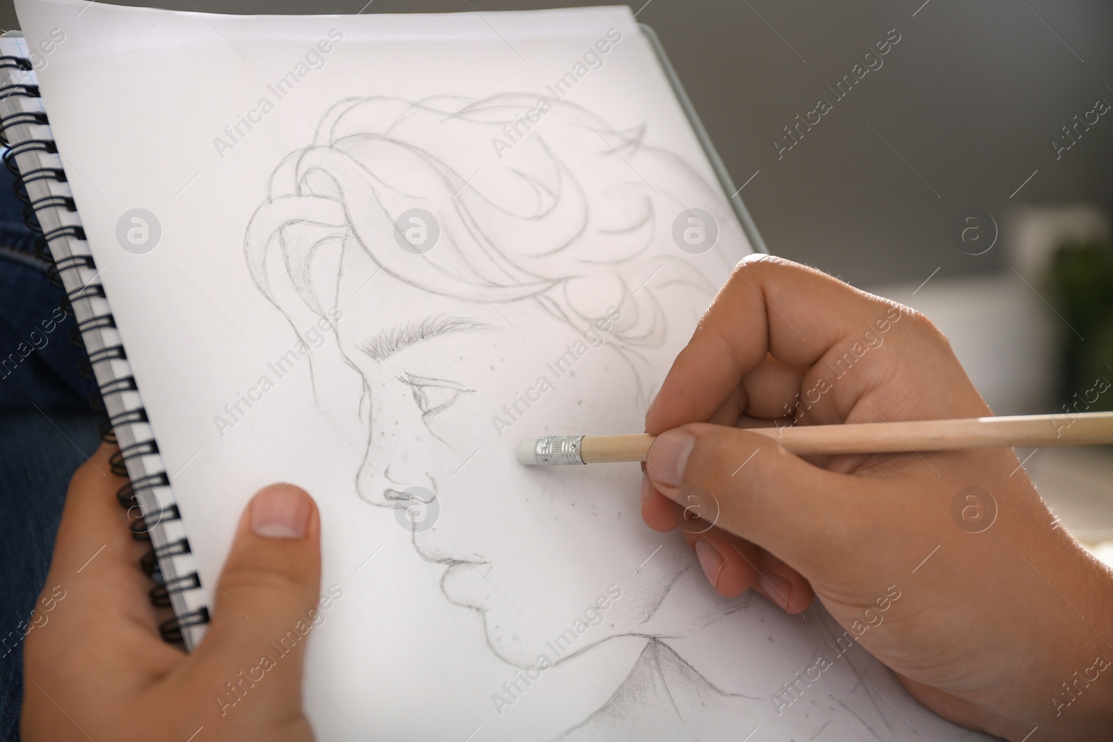 Photo of Man drawing portrait with pencil in notepad indoors, closeup