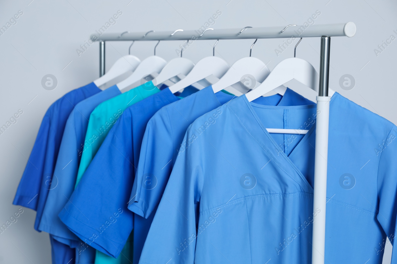 Photo of Different medical uniforms on rack against light grey background