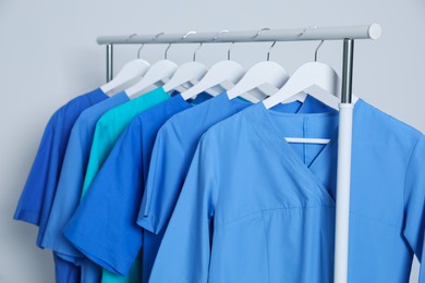 Photo of Different medical uniforms on rack against light grey background