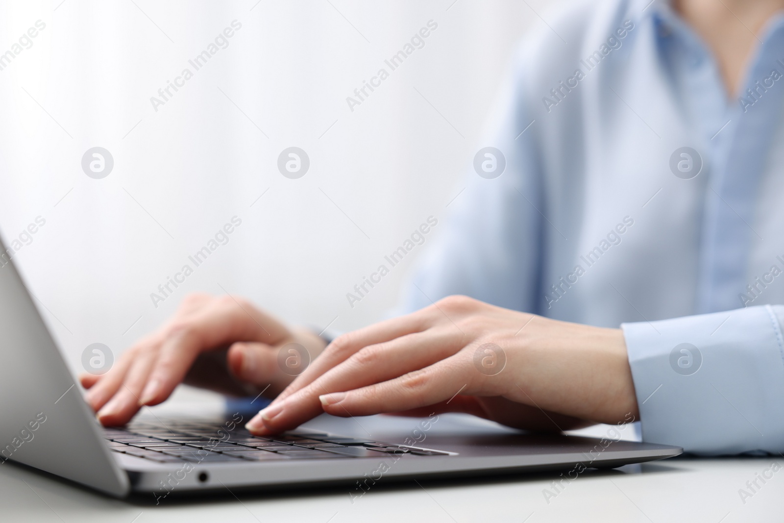 Photo of E-learning. Woman using laptop at white table indoors, closeup