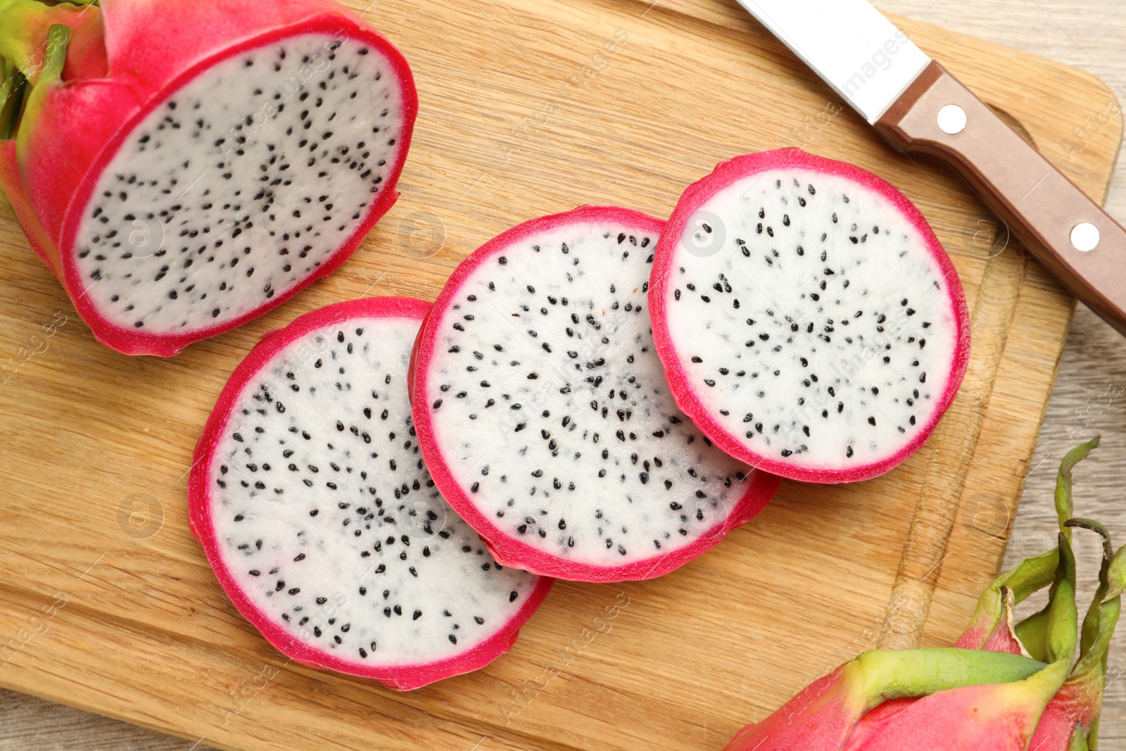 Photo of Delicious cut white pitahaya fruit and knife on wooden board, top view