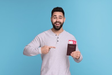 Photo of Happy man pointing at passport and tickets on light blue background