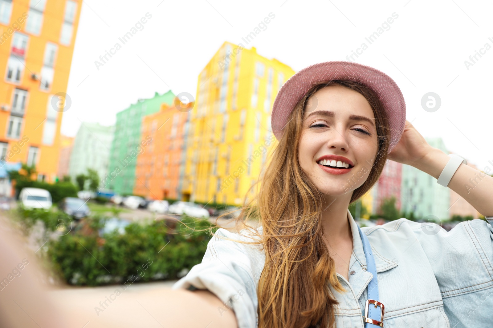 Photo of Beautiful young woman in stylish hat taking selfie outdoors