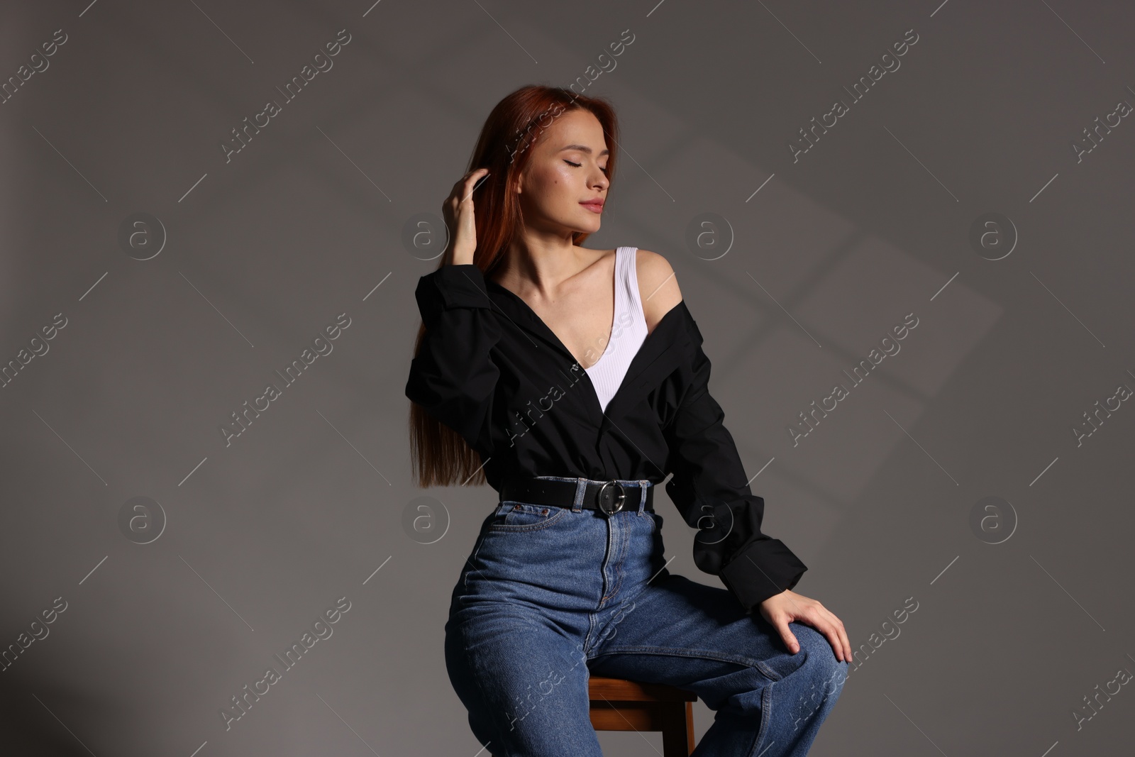 Photo of Beautiful young woman sitting on stool against gray background