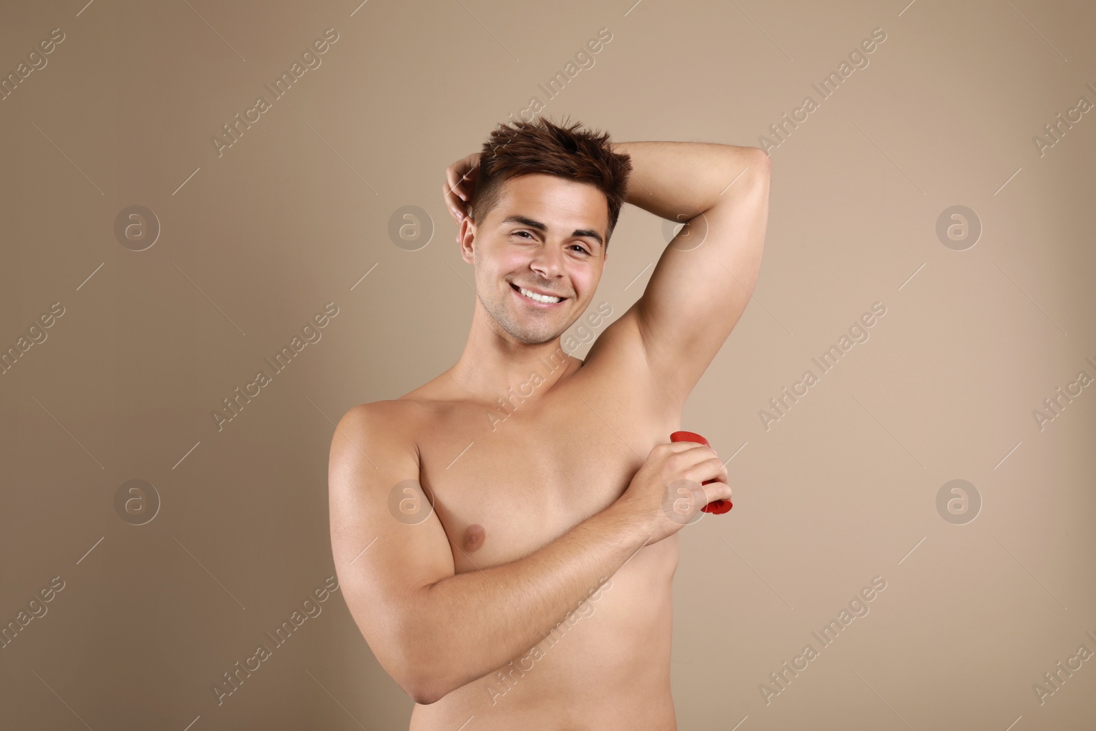 Photo of Young man applying deodorant to armpit on beige background