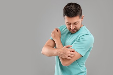 Photo of Allergy symptom. Man scratching his arm on light grey background. Space for text