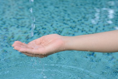 Photo of Water pouring into the girl's hand above pool, closeup