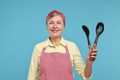 Photo of Happy housewife with spoons on light blue background