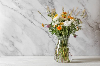 Bouquet of beautiful wild flowers and spikelets in vase on white wooden table. Space for text