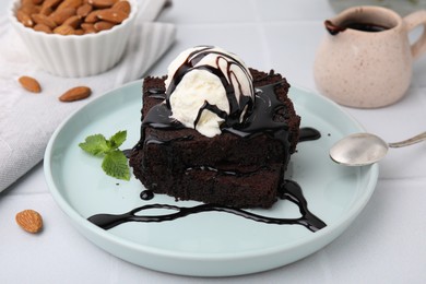 Photo of Tasty brownies served with ice cream and chocolate sauce on white tiled table, closeup