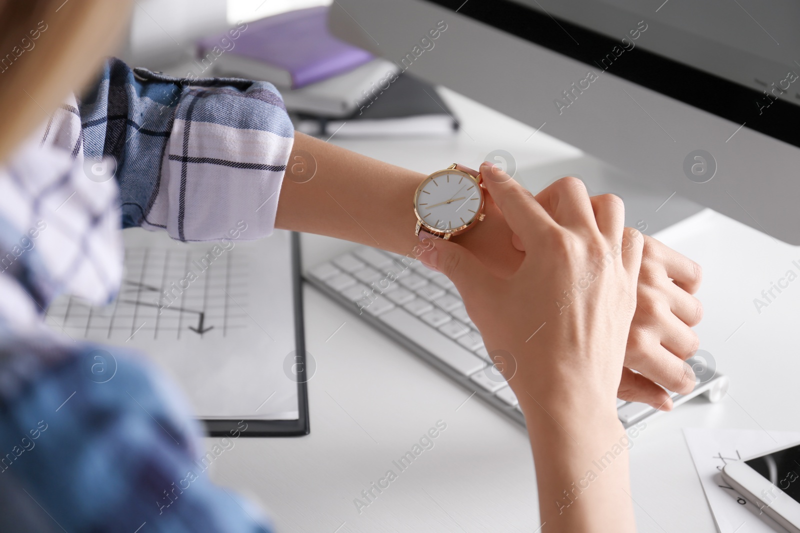 Photo of Young woman checking time on her wristwatch at workplace