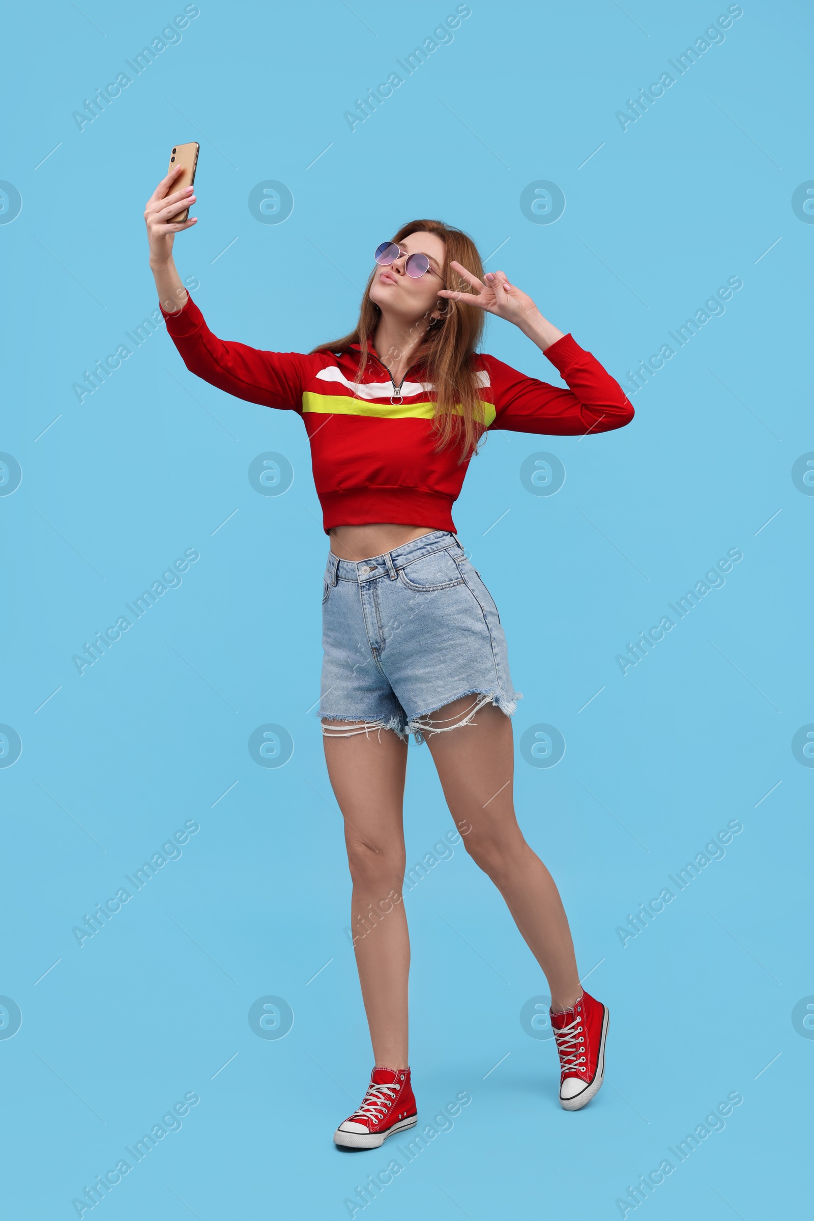 Photo of Beautiful woman in sunglasses taking selfie on light blue background