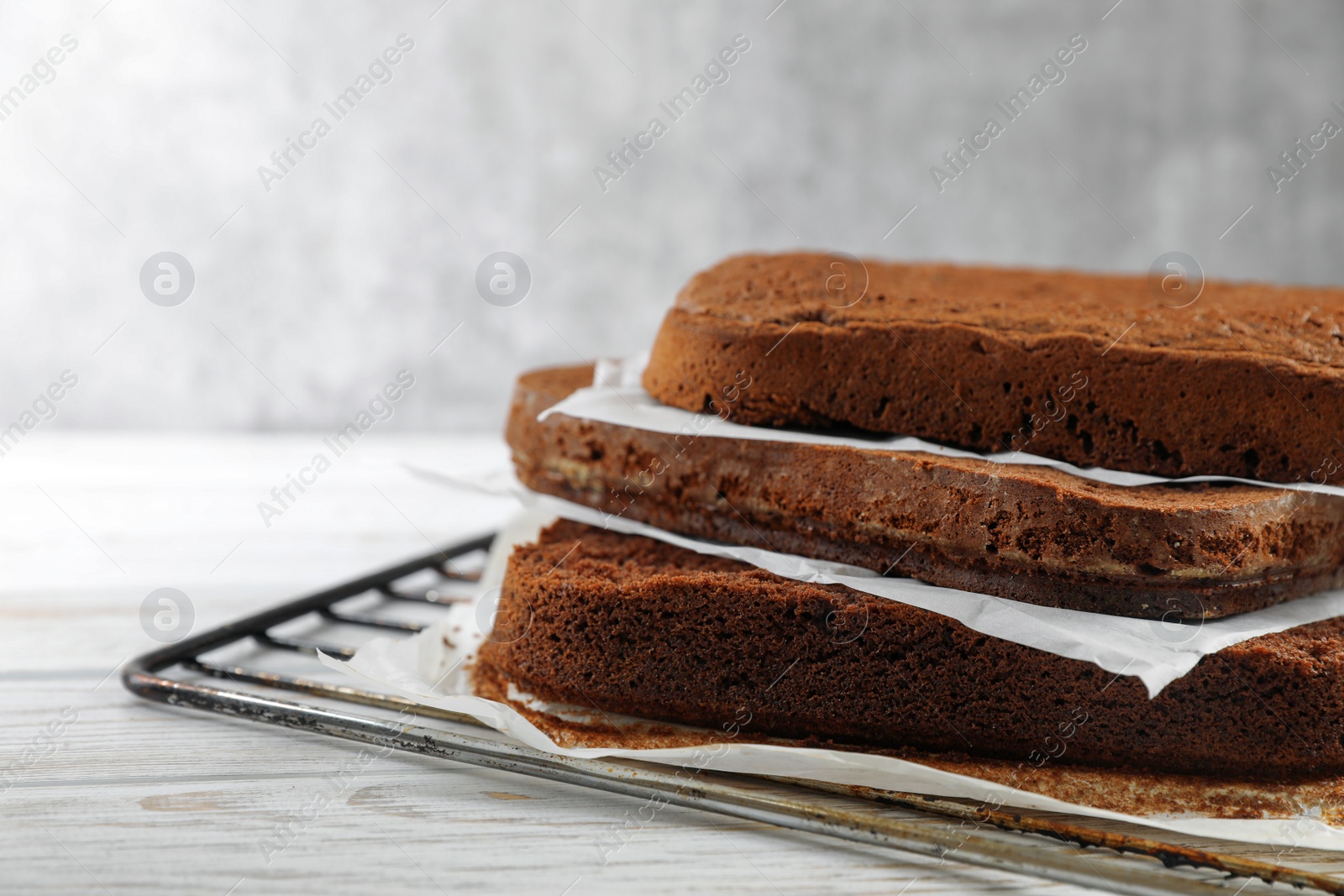 Photo of Layers of homemade chocolate sponge cake on white wooden table, closeup. Space for text