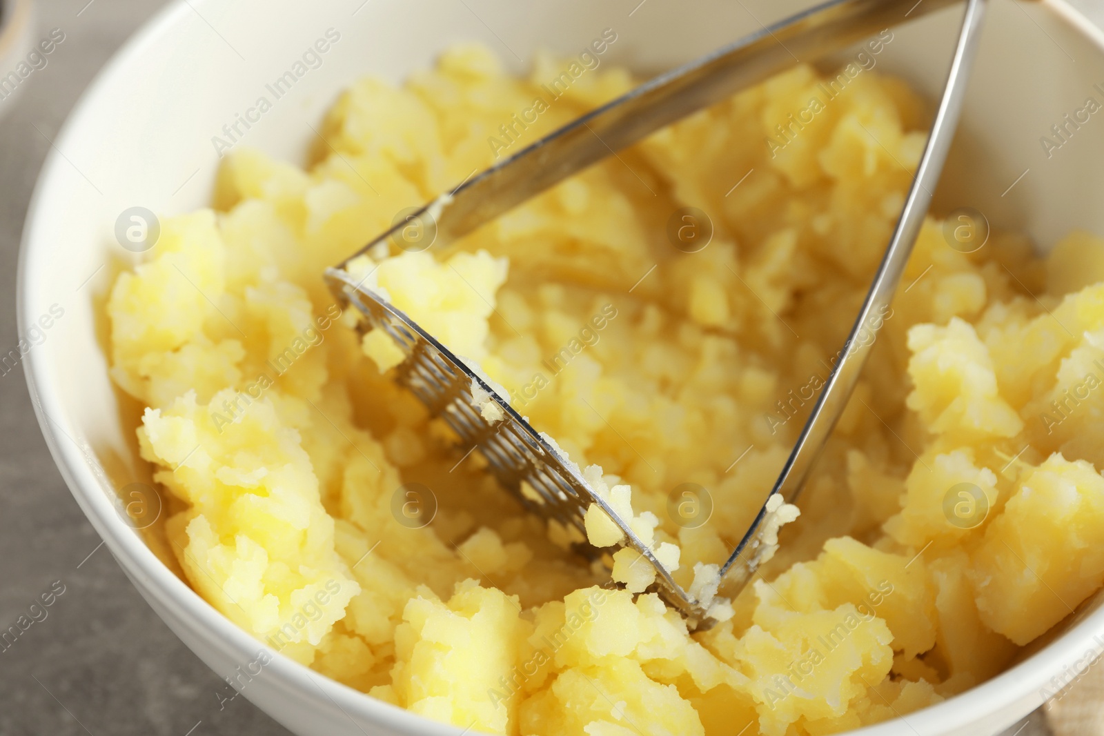 Photo of Bowl with delicious mashed potato and masher on light grey table, closeup