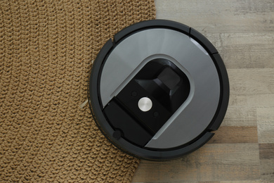 Photo of Modern robotic vacuum cleaner on knitted rug, top view