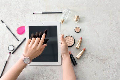 Photo of Young woman with makeup products using tablet at table. Beauty blogger