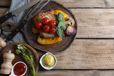 Delicious grilled meat and vegetables served with sauces on wooden table, flat lay. Space for text