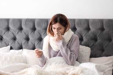 Sick woman with tissue and thermometer suffering from cold in bed