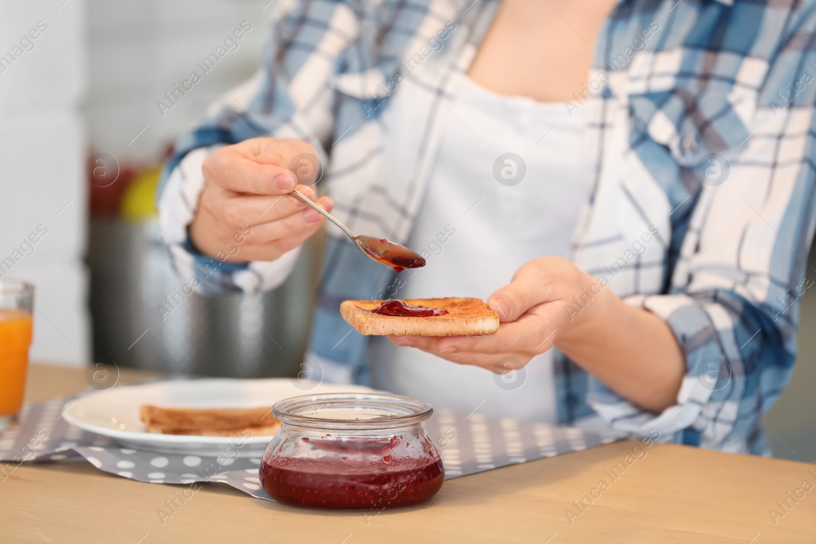 Photo of Beautiful woman spreading jam on toasted bread at table