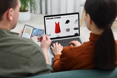 Photo of Couple with credit card and gadgets shopping online indoors, back view