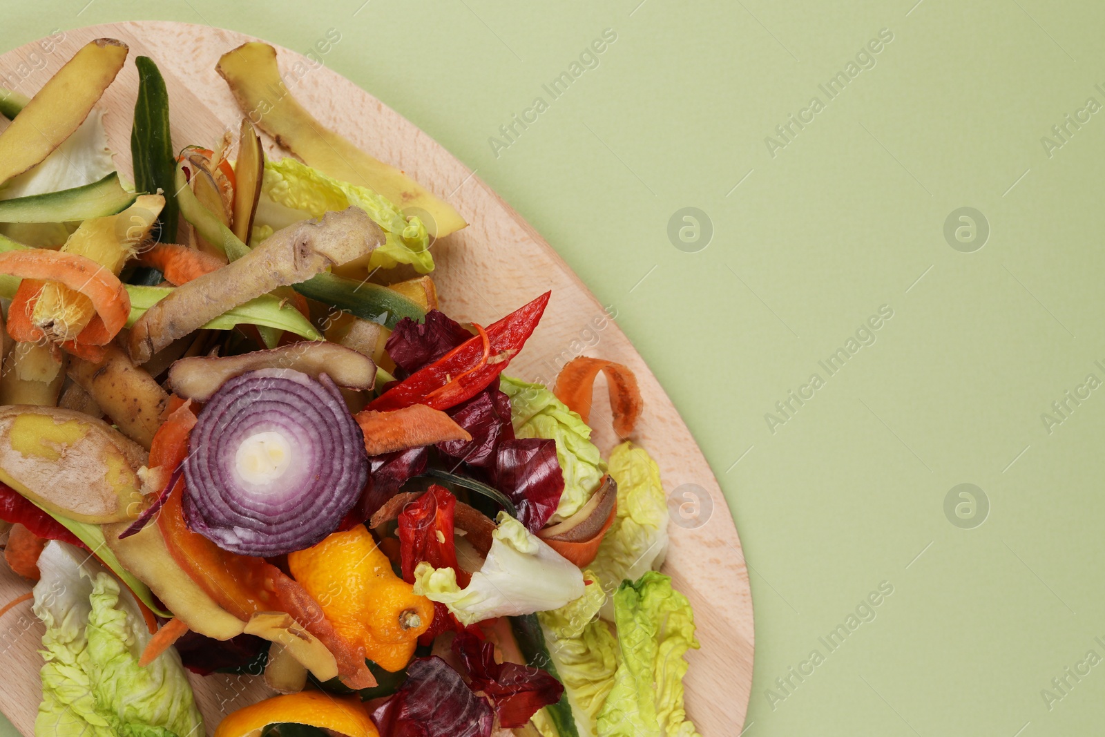 Photo of Peels of fresh vegetables with wooden board on light green background, top view. Space for text