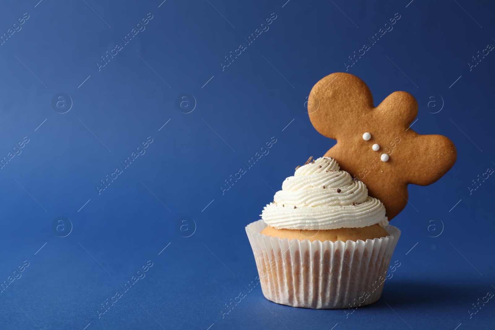 Photo of Tasty Christmas cupcake with cream and gingerbread man cookie on blue background, space for text