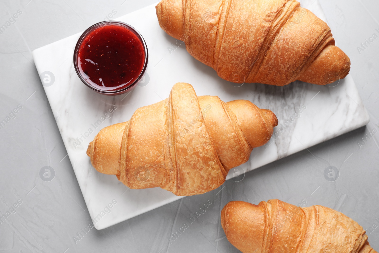 Photo of Tasty fresh croissants and jam on grey table, flat lay