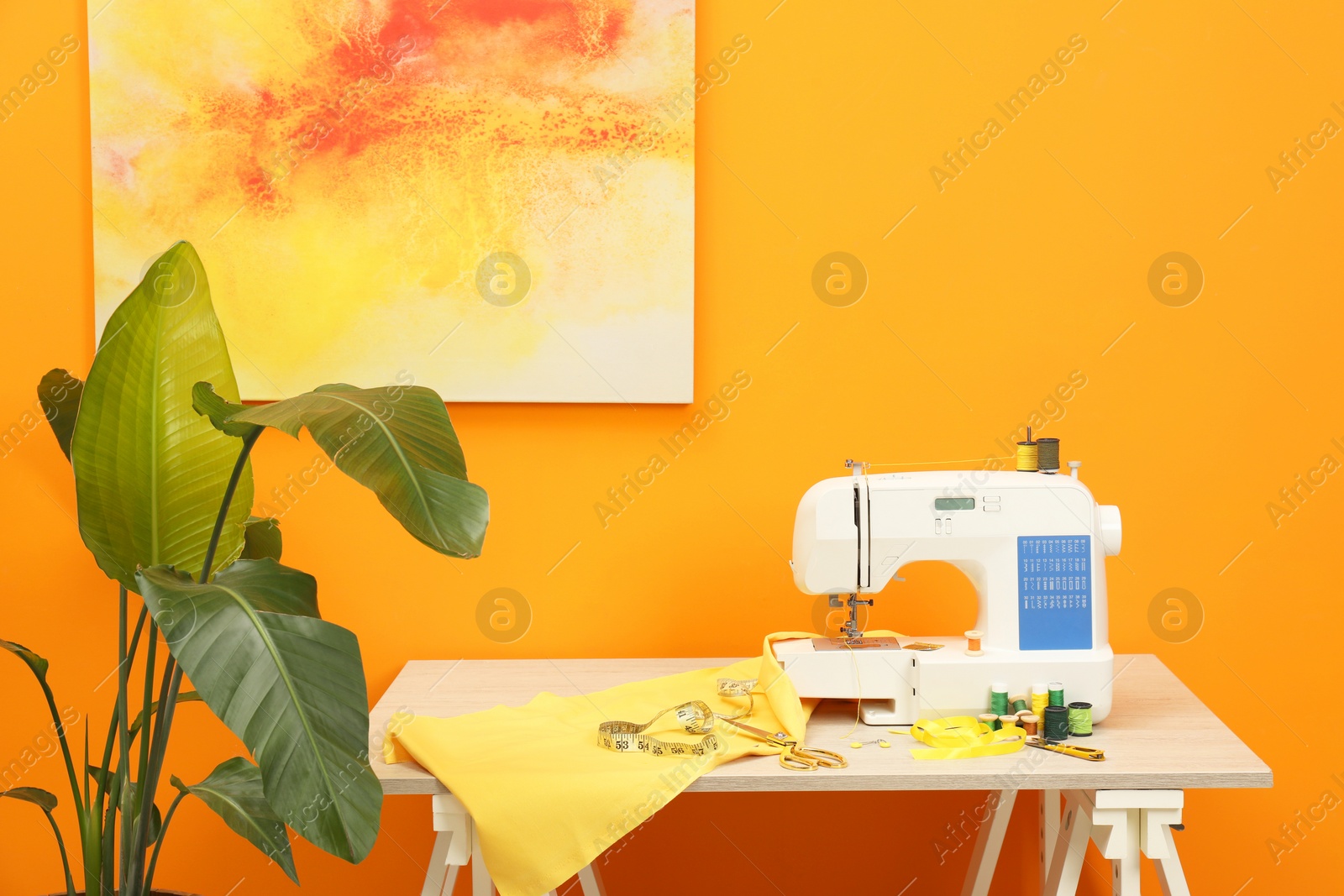 Photo of Modern sewing machine with cloth and craft accessories on wooden table near orange wall in room